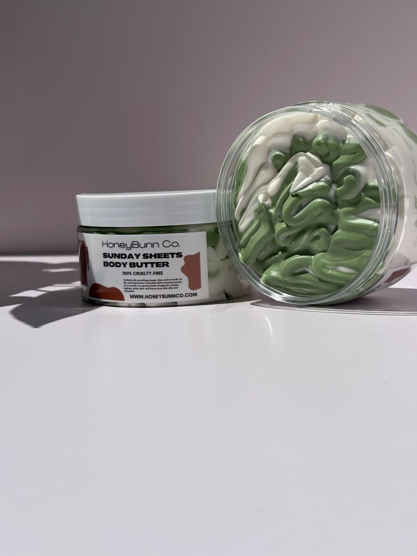 Two containers of Summer body butter, one open showing green product, on a white surface with a gray background.