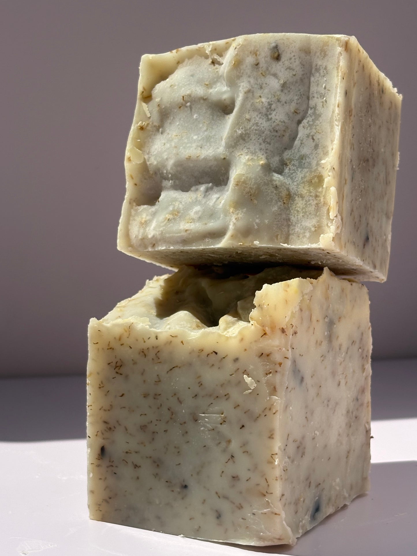 Two pieces of natural soap with a speckled texture on a gradient background