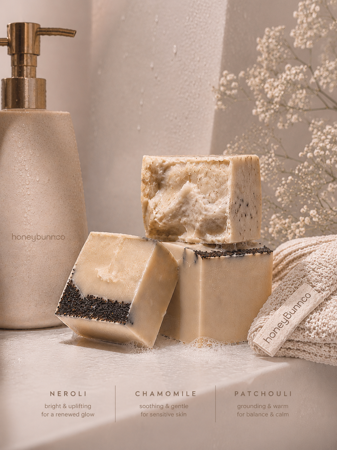 Three bars of soap with labels on a textured surface next to a soap dispenser.